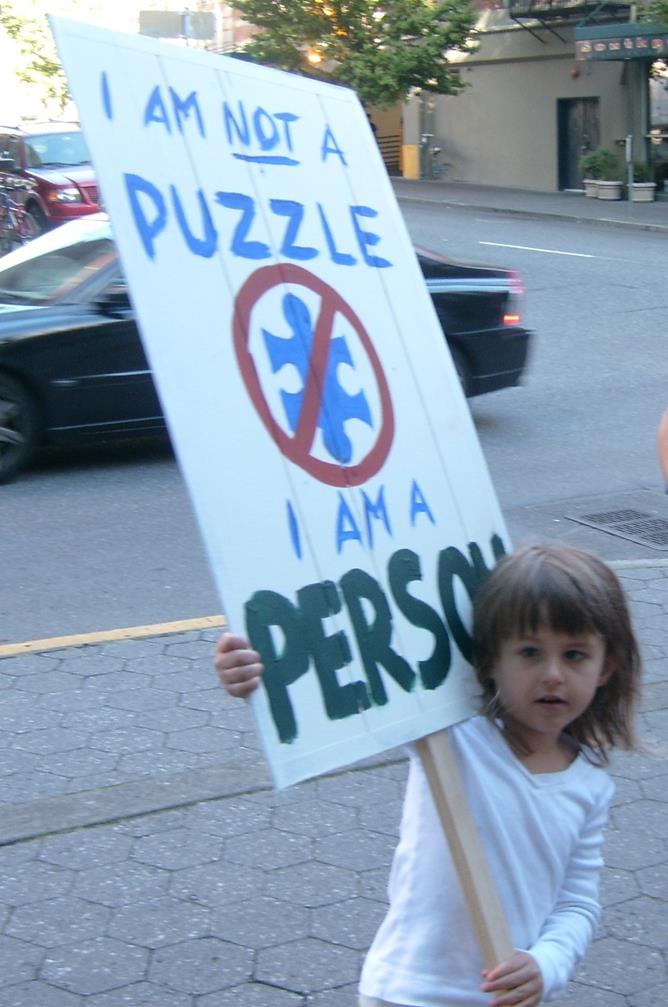 A young girl holds a protest sign that says "I am not a puzzle - I am a person"