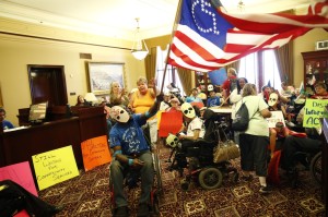 ADAPT fills an office - the ADAPT flag and many signs are visible - several read still Waiting for Community Services