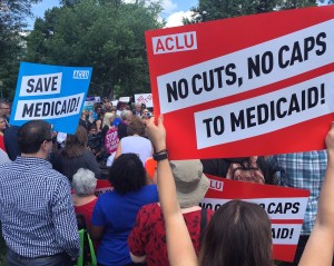 Approximately 50 people are gathered for a Rally. Several people have signs that read No Cuts No Caps to Medicaid - ACLU