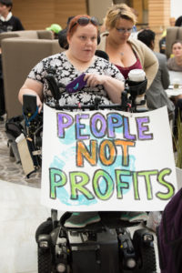 A NCIL member holds a sign that reads "People Not Profits" at the 2017 Annual Conference on Independent Living