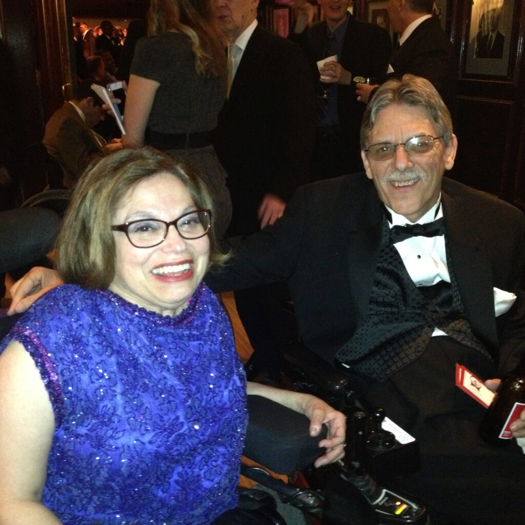 Kelly Buckland and Judy Heumann pose at the 2013 Inaugural Ball. They are wearing formal attire and are surrounded by other partygoers. 