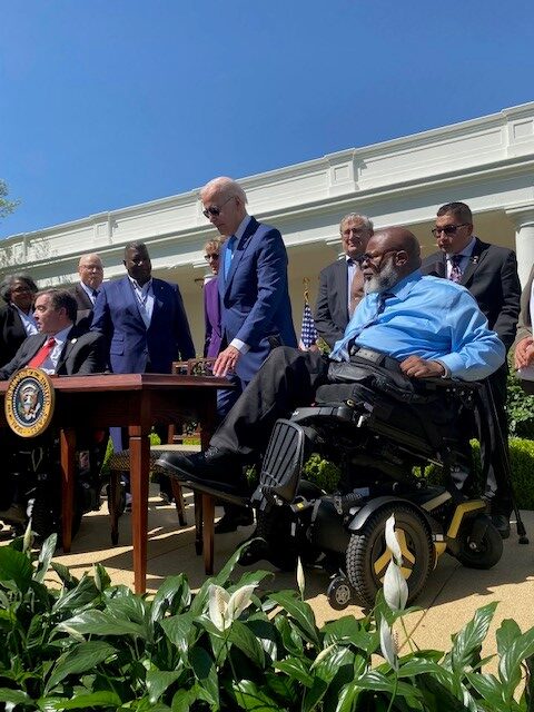 Theo Braddy sits to the left of President Biden as he signs the Executive Order from a table with the Presidential seal at the front. 